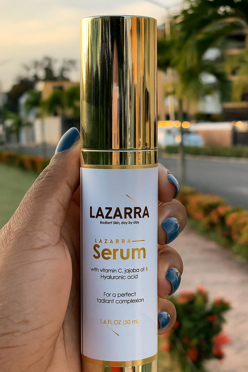 May include: A cylindrical serum bottle with a reflective gold cap and base. The white label features the text LAZARRA, Radiant Skin, day by day, LAZARRA Serum, with vitamin C, jojoba oil & Hyaluronic acid, For a perfect radiant complexion, 1.6 FL OZ (50 mL).