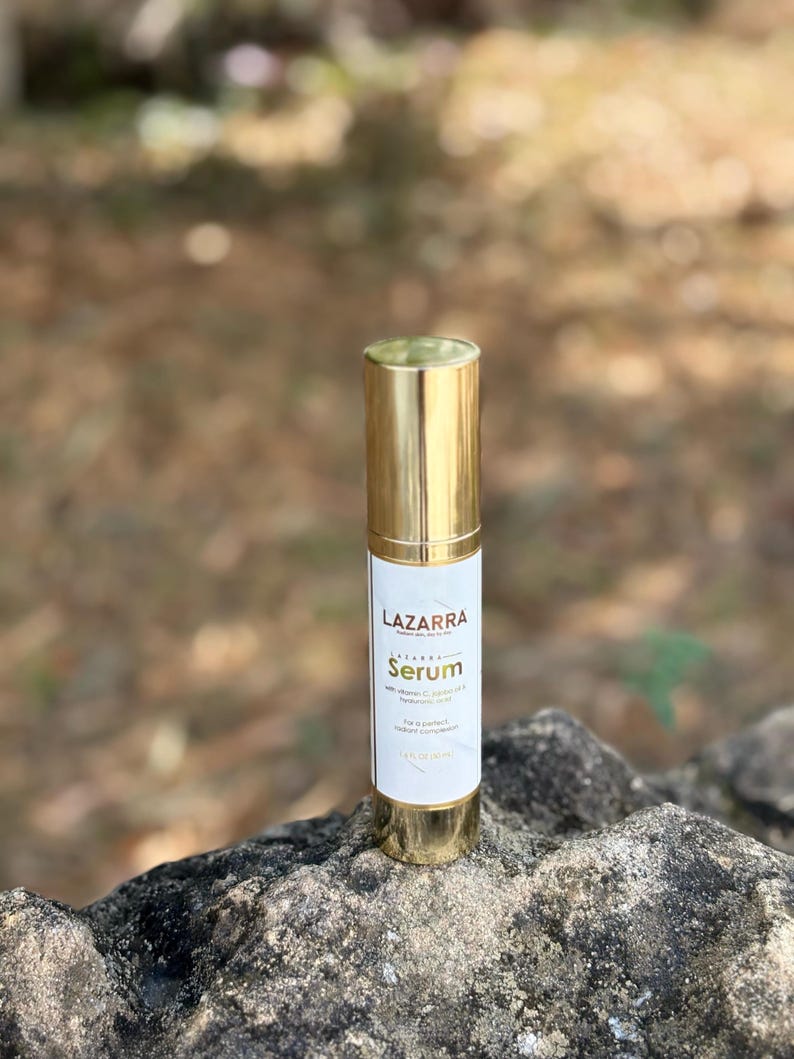 May include: A cylindrical bottle of Lazzara Serum with a metallic gold cap and base. The white label features the text Lazzara Serum with vitamin C, vitamin E & hyaluronic acid, for a perfect radiant complexion, and 1.0 FL OZ (30 ml).