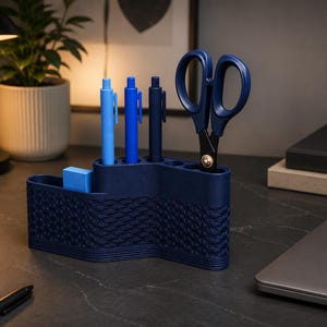 Op de afbeelding: Een marineblauwe bureau-organizer met een textuur golfpatroon, met blauwe pennen, een blauwe gum en een blauwe schaar. De organizer staat op een bureau met een laptop, notitieboek en een lamp.