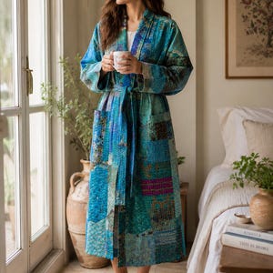 May include: A long-sleeved, calf-length robe featuring a patchwork design in various shades of blue, teal, and purple. The garment has a shawl collar, a matching fabric tie belt at the waist, and two front pockets, all finished with visible stitching.