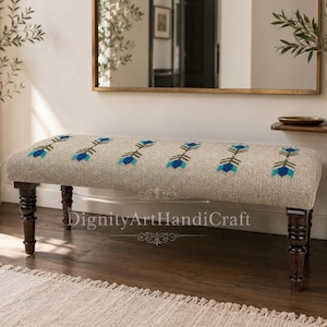 May include: A rectangular upholstered bench featuring a textured beige fabric with a repeating pattern of blue and green arrow-like motifs. The bench is supported by four dark brown turned wooden legs. The text DignityArtHandiCraft is visible.