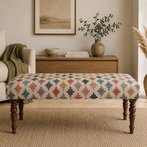 May include: A rectangular upholstered bench featuring a cream-colored fabric with a repeating geometric cross pattern in shades of red, blue, yellow, and gray. The bench is supported by four dark brown wooden legs with a turned, spindle-style design.