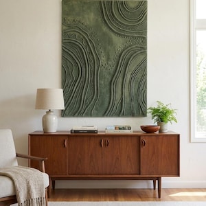 Peut inclure: Une œuvre d'art murale rectangulaire présentant une surface texturée vert sauge avec des lignes topographiques en relief et des motifs de petits points. L'œuvre est fixée sur un mur uni au-dessus d'un long buffet en bois à quatre portes.