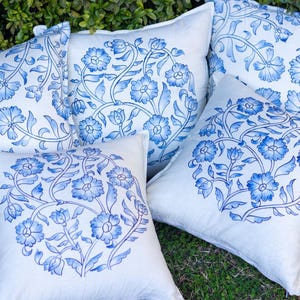 May include: Several white throw pillows with a blue floral design. The pillows are arranged together, showcasing the intricate patterns of flowers and leaves. The design is a detailed, hand-painted style, adding a touch of elegance to the home decor.
