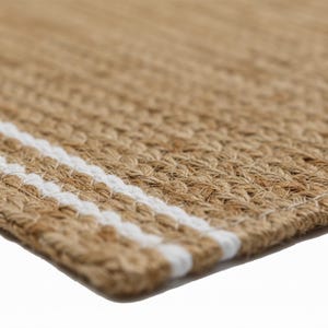 May include: Close-up of a natural fiber rug with a woven texture. The rug is primarily a light brown color with two bold white stripes running across the width. The rug's texture is visible, showcasing the natural fibers.