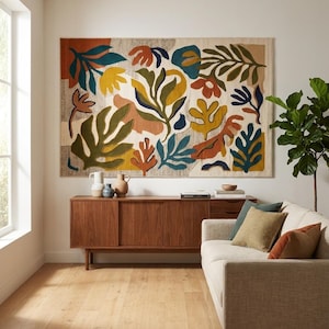 Könnte beinhalten: Ein großer rechteckiger Wandteppich mit einem abstrakten botanischen Muster aus organischen Blatt- und Blumenformen in Senfgelb, Olivgrün, Terrakotta und Dunkelblau, der über einem hölzernen Sideboard mit drei Keramikvasen angebracht ist.