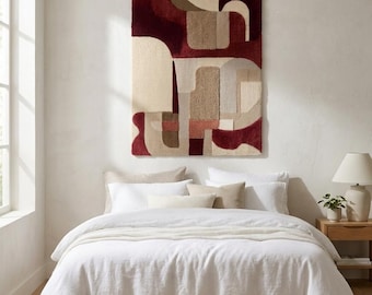 May include: A rectangular wall hanging featuring a tufted, abstract geometric pattern in deep burgundy, cream, beige, and muted brown tones. The textile art displays a mix of curved and straight shapes with varying pile heights and textures.