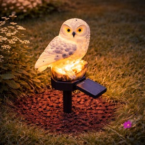 Puede incluir: Una estatua de búho de jardín con energía solar con una luz cálida y brillante. El búho blanco tiene ojos amarillos y está sobre una base de madera artificial. Un pequeño panel solar está unido a la estaca negra, ideal para la decoración exterior.