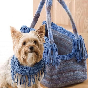 Könnte beinhalten: Ein kleiner Hund mit einem blauen Fransen-Schal steht neben einer blau-grauen Strick-Tragetasche mit Fransen. Die Tasche hat zwei Griffe und ein strukturiertes Aussehen, was auf einen handgefertigten Artikel hindeutet.
