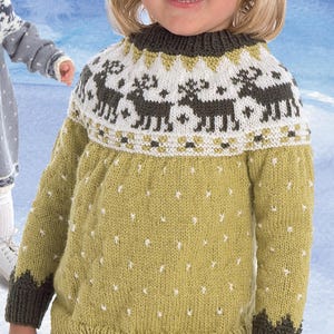 以下が含まれることがあります： 白い水玉模様と、ヨークにトナカイ模様が入ったオリーブグリーンの子供用ニットセーター。セーターは濃い緑色の袖口と濃い緑色の襟が付いています。子供はオリーブグリーンのズボンを履いています。