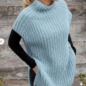 Puede incluir: Un poncho de punto azul claro con textura acanalada. El poncho tiene un cuello alto y redondo y mangas cortas. Se lleva sobre una camisa negra de manga larga. La prenda tiene aberturas laterales y un corte holgado.