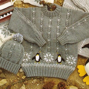 May include: A gray knitted sweater and matching beanie featuring a penguin and snowflake design. The sweater has a crew neck and long sleeves. The beanie has a pom-pom on top. The set is perfect for winter.