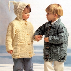 May include: Two children's knitted coats. One is cream-colored with a hood and wooden toggle closures. The other is a dark teal color with a collar and wooden toggle closures. Both coats have pockets and cable knit detailing.