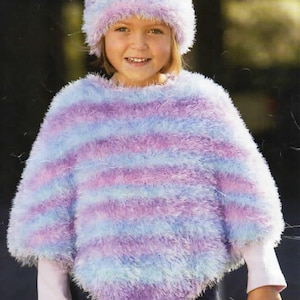 May include: A child wearing a fluffy, striped poncho and matching hat. The poncho and hat are in shades of blue, purple, and pink. The child is also wearing a long-sleeved white shirt underneath the poncho. The clothing appears to be handmade.