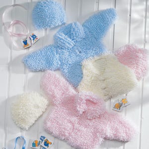 May include: A collection of soft, fluffy baby clothing sets in pastel colors. The sets include a jacket and a matching hat. The jackets are light blue, pink, and cream. The items are arranged on a white wooden surface.