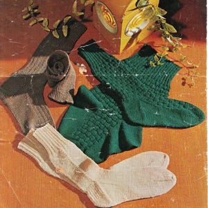 May include: A selection of knitted socks in shades of green, beige, and brown. The socks are displayed on an orange surface, some folded and others spread out. The socks feature diverse patterns and textures, showcasing a variety of styles.