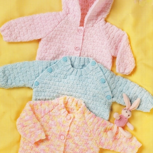 May include: Three knitted baby cardigans in pastel shades: a pink hooded one, a light blue one, and a multi-coloured pink and yellow one. Each has button fastenings. A small pink bunny toy is next to the multi-coloured cardigan.