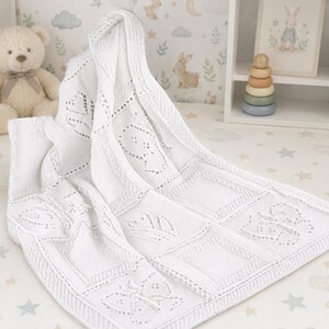 May include: A white knitted baby blanket featuring a repeating pattern of butterflies and leaves created with openwork eyelet stitches. The blanket has a textured border and a soft, woven construction with a consistent white color throughout the fabric.