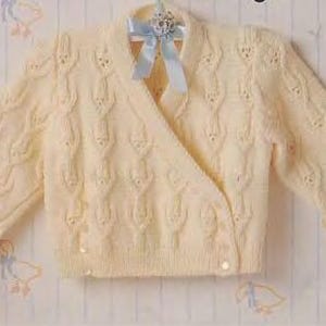 May include: A cream-colored, knitted baby cardigan with a wrap-style front and long sleeves. The sweater features a textured pattern and is fastened with small buttons. A light blue ribbon is attached to the hanger.
