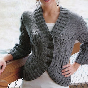 May include: A gray knitted cardigan with a V-neck and button closure. The sweater features cable knit and ribbed detailing, with a tailored fit. The sleeves are three-quarter length. The cardigan is worn over a white top.