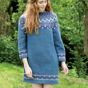 May include: A blue knit dress with a patterned yoke, cuffs, and hem. The pattern includes white, red, and blue geometric shapes. The dress has long sleeves and a crew neck. The model is standing in a grassy area.