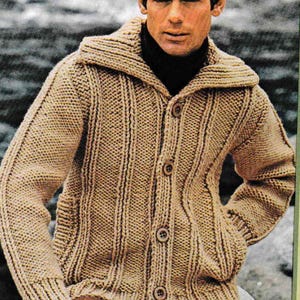 May include: A tan, knitted cardigan sweater with a shawl collar and button closure. The sweater has vertical ribbed detailing and two front pockets. The person in the image is wearing a black turtleneck underneath.