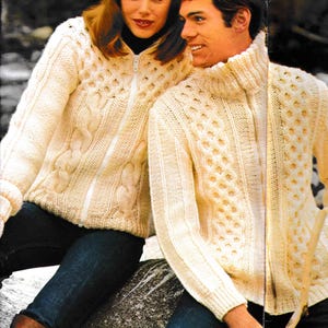 May include: Cream-colored knitted zip-up sweaters with cable knit and textured patterns. The sweaters have high collars and are paired with dark blue jeans. The image shows a couple wearing the sweaters.