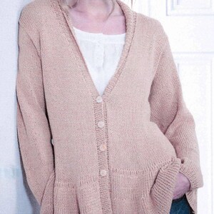 May include: A light pink cardigan with a V-neck and button closure. The long-sleeved sweater has a flared hem and is worn over a white blouse. The model is wearing blue jeans.