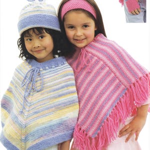 Könnte beinhalten: Zwei junge Mädchen tragen gestrickte Ponchos und Hüte. Eines trägt einen blau, gelb und weiß gestreiften Poncho und einen passenden Hut. Das andere trägt einen rosa und weiß gestreiften Poncho mit einem rosa Stirnband. Die Ponchos haben Fransen.