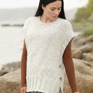 Puede incluir: Un chaleco de punto gris claro con cuello redondo y mangas cortas. El chaleco tiene un dobladillo acanalado y aberturas laterales, abrochado con tres botones grandes, redondos y de color marrón claro. La modelo lleva debajo una camisa marrón de manga larga.