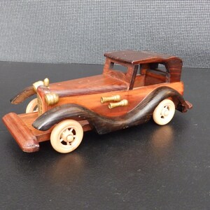 May include: A wooden model of a vintage car. The car is primarily brown with dark brown fenders and a dark brown roof. It has cream-colored wheels and brass-colored accents. The model is a detailed replica of a classic automobile.