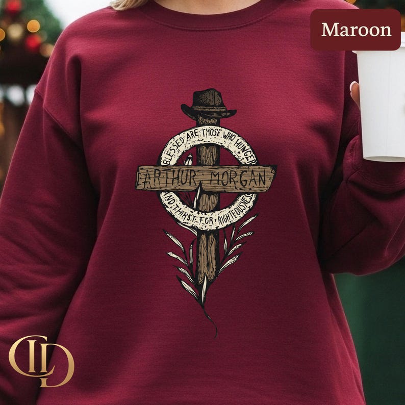 May include: Maroon sweatshirt with a cross graphic. The design includes the text "ARTHUR MORGAN" and the quote "Blessed are those who hunger and thirst for righteousness." The graphic also features a hat and floral elements.