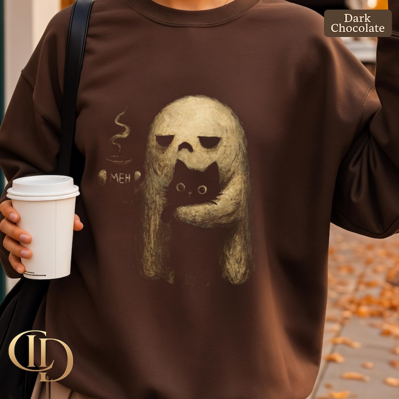 May include: Dark chocolate brown sweatshirt featuring a whimsical illustration of a ghost embracing a black cat. The ghost has a skull-like face and the cat has large, round eyes. A coffee cup with the word "MEH" is also visible.