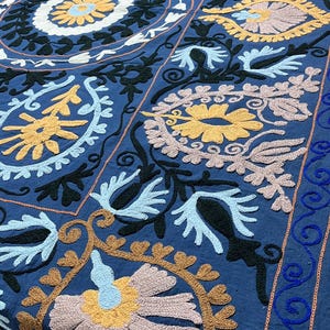 Può includere: Un grande tessuto blu con intricati motivi floreali ricamati a mano in tonalità giallo, azzurro, nero e rosa tenue. Il design presenta un motivo circolare centrale circondato da forme ripetitive simili al paisley e motivi a viticcio.