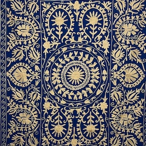 Può includere: Un tessuto blu intenso caratterizzato da un intricato ricamo color oro. Il design presenta un medaglione circolare centrale circondato da motivi floreali e fogliari simmetrici, racchiuso in un bordo rettangolare con motivi a onde ripetuti.
