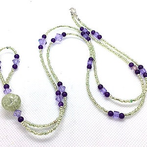 May include: A double-strand necklace with a light green and silver bead, and purple and light purple glass beads.