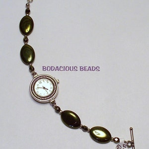 May include: A silver watch with a white face and black hands on a green beaded bracelet. The bracelet has a silver clasp and a tag that says "Watch Green".