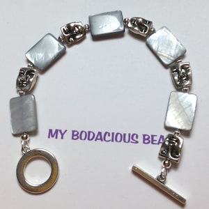 May include: A silver bracelet with a toggle clasp. The bracelet features alternating silver face beads and iridescent gray rectangular beads.