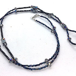 May include: A double-strand necklace made with black and silver beads. The necklace features iridescent beads and square-shaped silver beads.