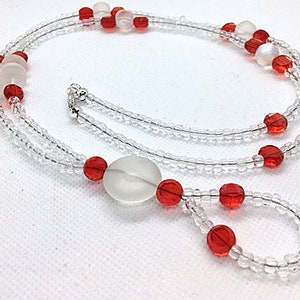 May include: A double-strand beaded necklace with clear and red beads. The necklace features a large, opaque white bead.