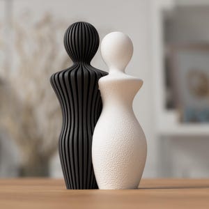 May include: A black and white decorative sculpture of two figures. The black figure has a vertical striped design, while the white figure has a textured surface. The figures are standing close together.