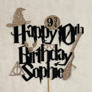 May include: A black and gold glitter cake topper with the words "Happy 10th Birthday Sophie". The topper includes a sorting hat, 9 3/4 sign, glasses, broom, and other themed elements.