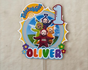 Può includere: Un colorato cake topper con i personaggi dei Teletubbies. Il design include la parola "Teletubbies" in giallo, il numero "1" in azzurro e il nome "Oliver" in un font multicolore, con decorazioni floreali. Lo sfondo mostra i Teletubbies in un cerchio.