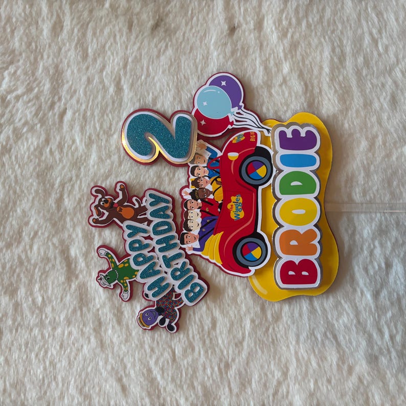 Pu&ograve; includere: Decorazione colorata per torta di compleanno con un'auto rossa, personaggi dei Wiggles, il nome "Brodie" e il numero "2". Include un messaggio "Buon Compleanno" e decorazioni a palloncino. Perfetto per una festa di compleanno per bambini.