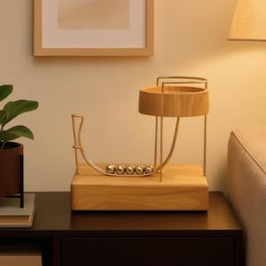 Könnte beinhalten: Ein Newton-Wiege-Schreibtischspielzeug aus Holz und Gold. Die Basis ist rechteckig und trägt einen gebogenen Goldrahmen und einen kreisförmigen Holzhalter. Sechs Metallkugeln liegen in einer Reihe. Das Design ist modern und minimalistisch.
