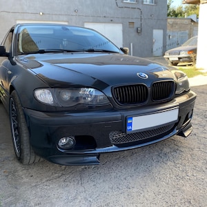 Könnte beinhalten: Ein schwarzer BMW-Pkw mit schwarzem Kühlergrill und Scheinwerfern. Das Auto hat ein Nummernschild mit blauen und gelben Farben. Das Auto steht auf einer Betonoberfläche.