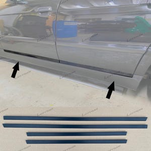 Puede incluir: Un juego de cuatro molduras laterales negras para puertas de coche. La imagen muestra dos tiras más largas y dos más cortas, diseñadas para su instalación a lo largo de los paneles inferiores de la carrocería, indicadas por flechas negras.