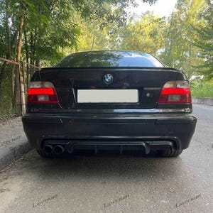 May include: A black BMW sedan viewed from the rear, featuring a prominent trunk lid spoiler, a central BMW emblem, horizontal red taillights, a blank license plate area, and a lower bumper diffuser with dual exhaust pipes on the left side.
