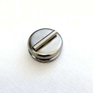 May include: A silver-colored, circular object with a cylindrical handle. The object appears to be made of metal and has a shiny, reflective surface. The handle is positioned across the top of the circle.