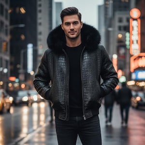 Op de afbeelding: Een zwarte leren jas met een met bont gevoerde capuchon, een zwarte trui en een zwarte jeans. De jas heeft een krokodillenleertextuur. De persoon staat op een natte straat in een stedelijke omgeving.